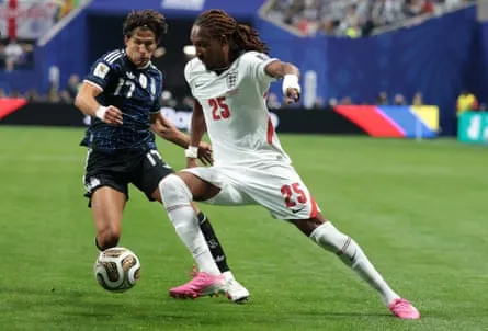 Djed Spence of England wearing a white jersey dribbles past an Argentina player wearing a blue jersey.