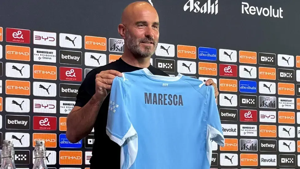 Enzo Maresca holding up a Man City shirt at his first news conference